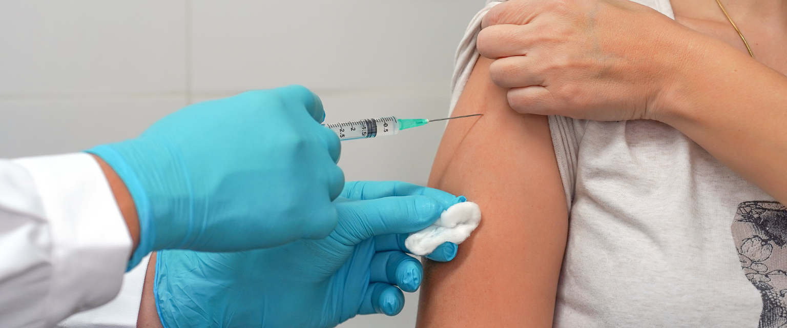patient getting a flu shot in their shoulder from a medical professional wearing blue gloves